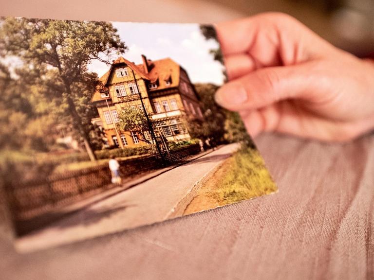 Eine Hand hält eine Postkarte mit der Ansicht der Kinderheilanstalt Waldhaus in Bad Salzdetfurth.
