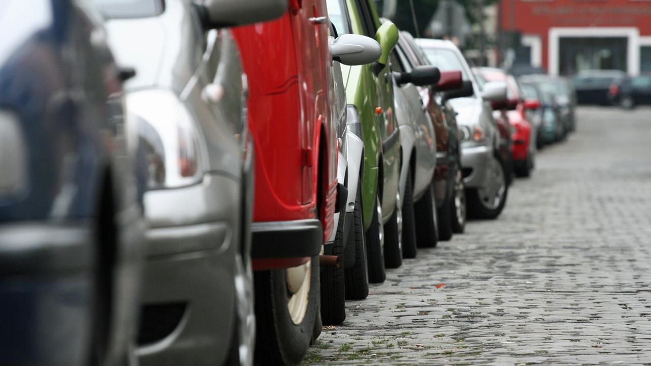 Auf einer Straße mit Kopfsteinpflaster in Köln parkt eine lange Reihe von Autos.