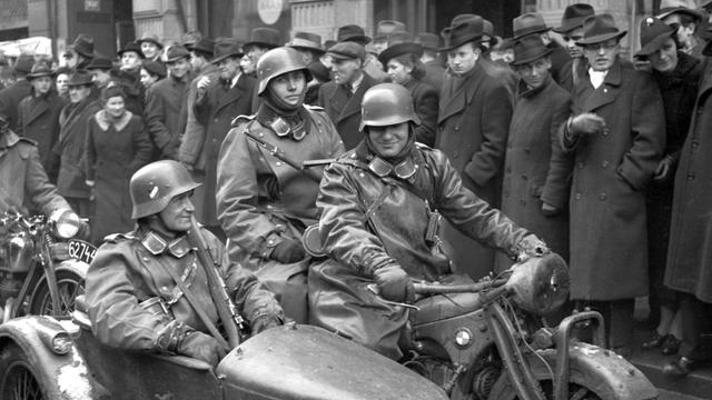 Zwei Soldaten auf dem Motorrad, einer im Beiwagen, fahren durch eine von Menschen gesäumte Straße in Prag