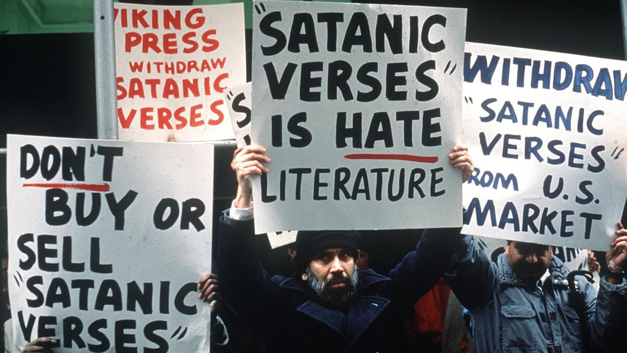 Mehrere muslimische Demonstranten halten Plakate hoch, auf denen das Buch "Satanische Verse" verurteilt wird. Mehrere muslimische Demonstranten halten Plakate hoch, auf denen das Buch "Satanische Verse" verurteilt wird.