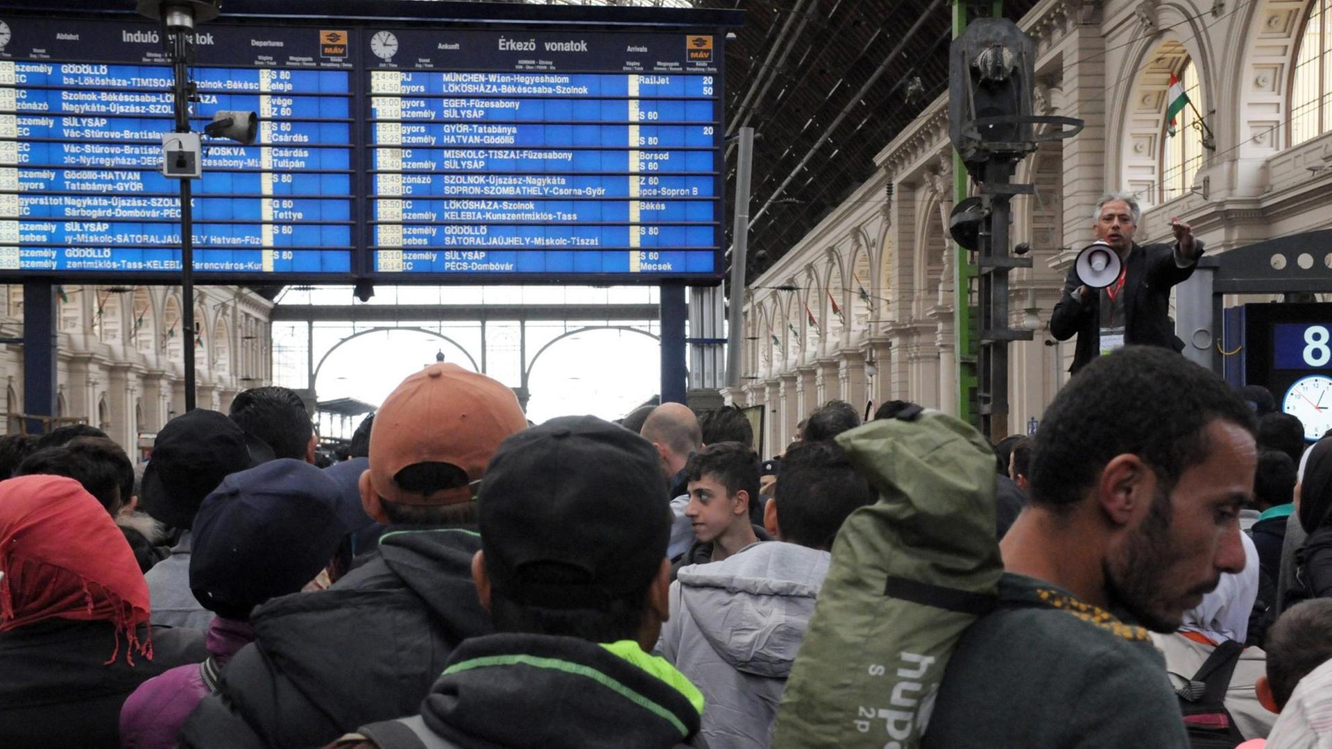 Flüchtlinge stehen auf dem Ostbahnhof in Budapest und hören einem Man mit Megafon zu. Flüchtlinge stehen auf dem Ostbahnhof in Budapest und hören einem Man mit Megafon zu.
