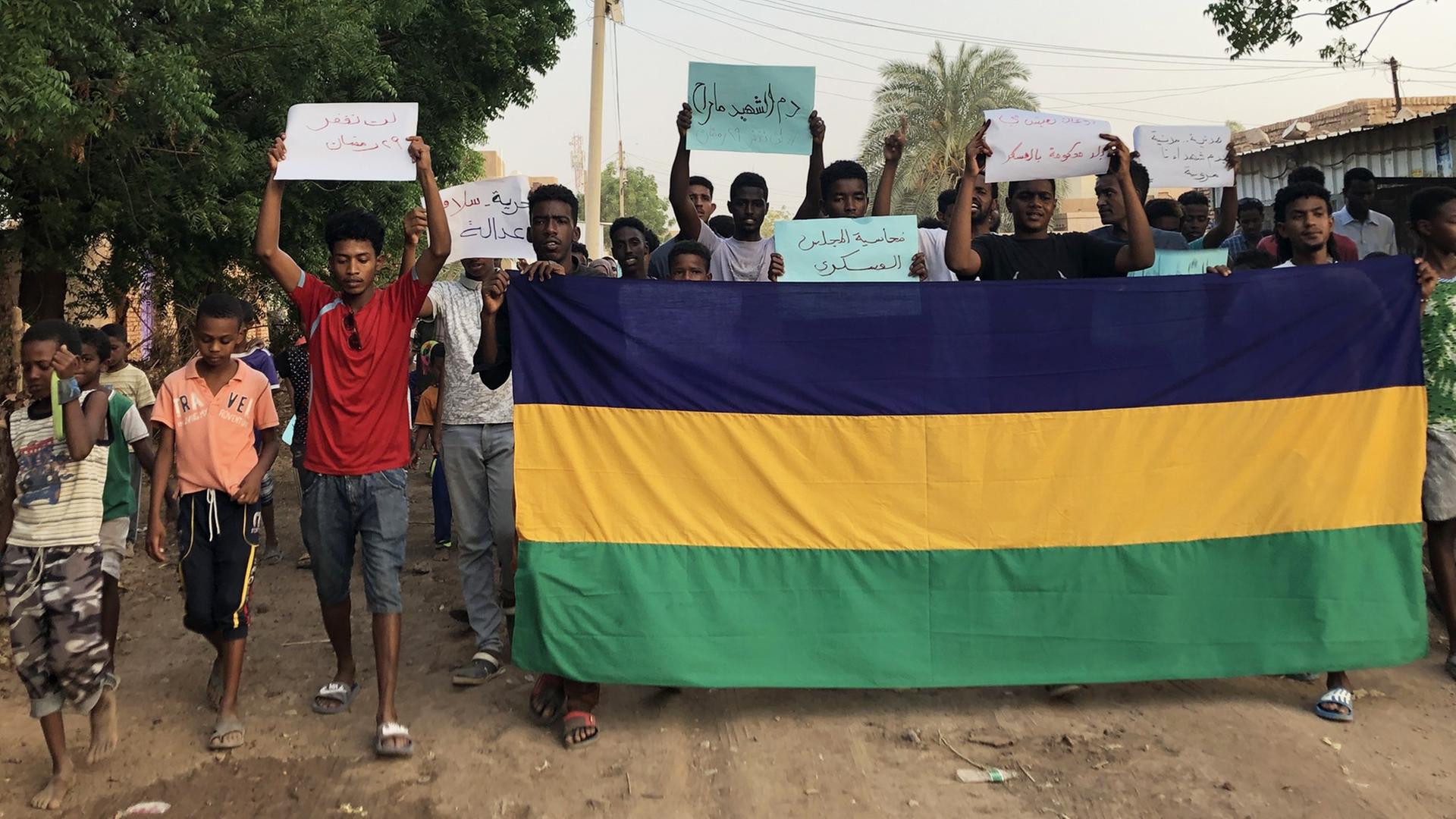 Jugendliche mit einer großen sudanesischen Fahne auf einer Landstraße halten Protestplakate hoch Jugendliche mit einer großen sudanesischen Fahne auf einer Landstraße halten Protestplakate hoch
