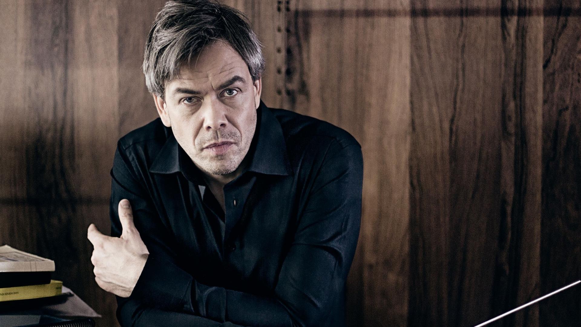 Hannu Lintu, an einem Schreibtisch sitzend mit Dirigierstab in der Hand Hannu Lintu, an einem Schreibtisch sitzend mit Dirigierstab in der Hand