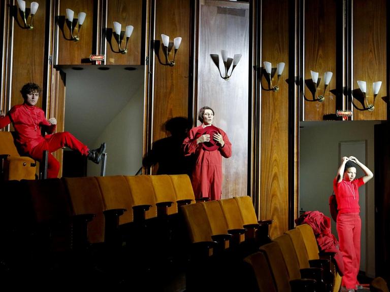 Eine Szene aus "Die Befristeten" am Schauspielhaus Bochum. Die Schauspieler*innen Dominik Dos-Reis, Marius Huth und Gina Haller stehen mit Abstand im leeren Zuschauerraum aufgereiht, in rot angezogen.