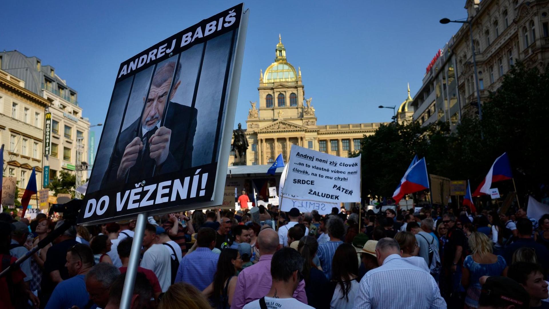 Demonstranten in Prag zeigen Schilder bei einem Protest gegen Regierungschef Babis. Auf einem ist er hinter Gittern zu sehen.