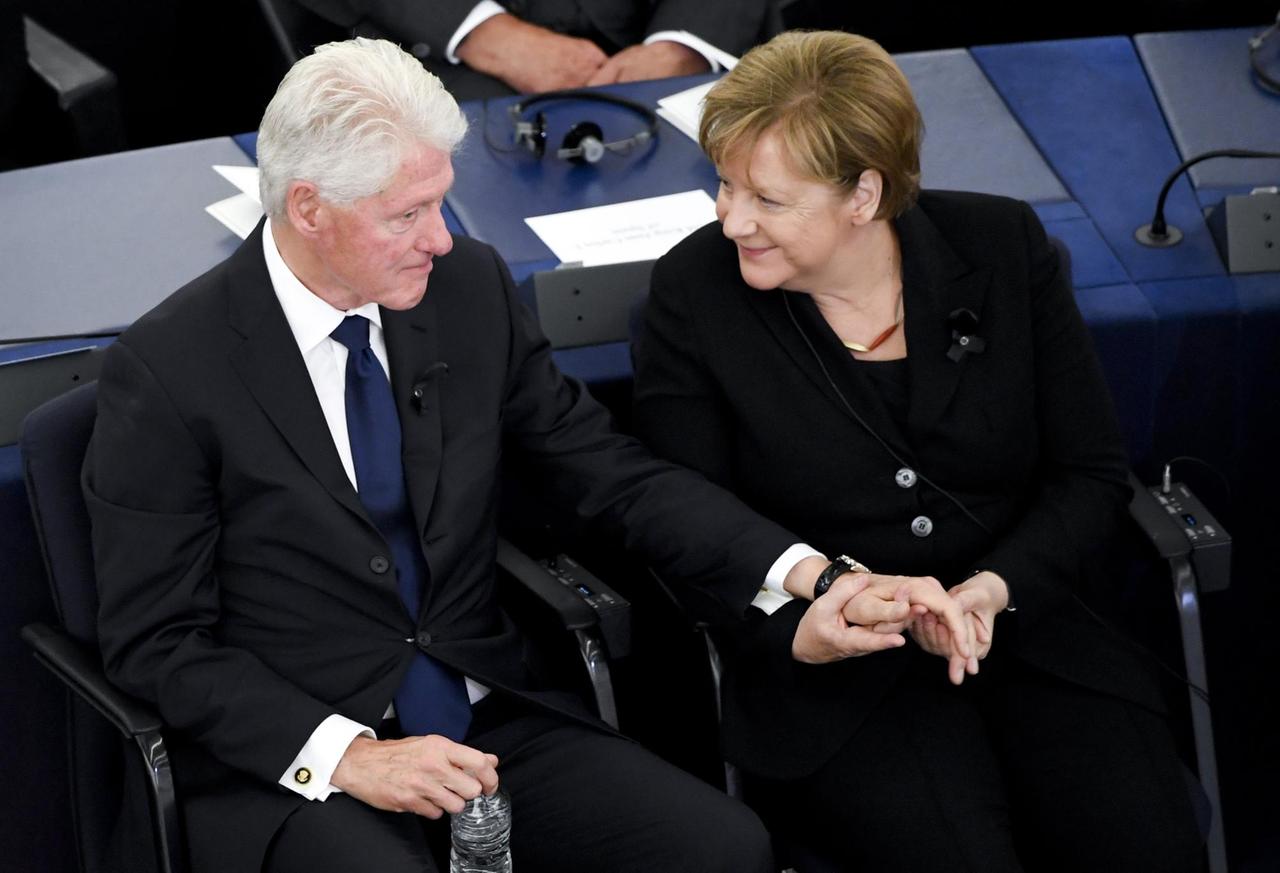 Der frühere US-Präsident Bill Clinton und Bundeskanzlerin Angela Merkel (CDU) sitzen am 01.07.2017 am europäischen Trauerakt für den verstorbenen Altkanzler Helmut Kohl im EU-Parlament in Straßburg nebeneinander. Clinton hat seine Hand auf der Merkels. 
