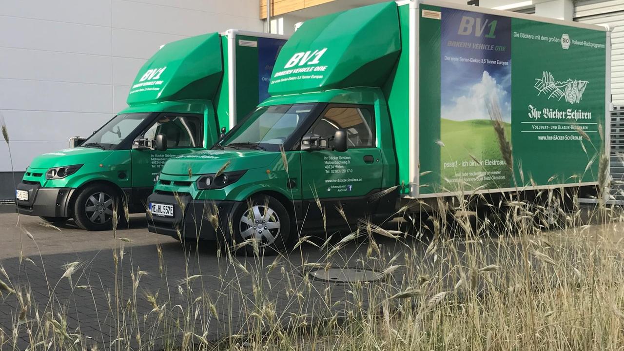 Zwei elektrisch angetriebene Lieferwagen der Bäckerei Schüren stehen auf dem Firmengelände. Sie sind in einem kräftigen Grün gestrichen, die Modellbezeichnung BV1 ist an mehreren Stellen deutlich zu lesen. Zwei elektrisch angetriebene Lieferwagen der Bäckerei Schüren stehen auf dem Firmengelände. Sie sind in einem kräftigen Grün gestrichen, die Modellbezeichnung BV1 ist an mehreren Stellen deutlich zu lesen.