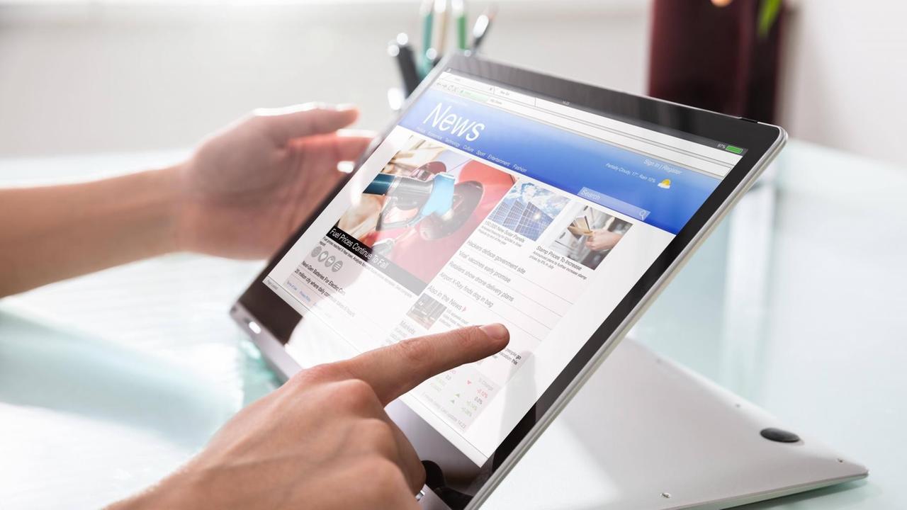 Eine Person liest auf einem Tablet einer Nachrichtenwebsite Eine Person liest auf einem Tablet einer Nachrichtenwebsite