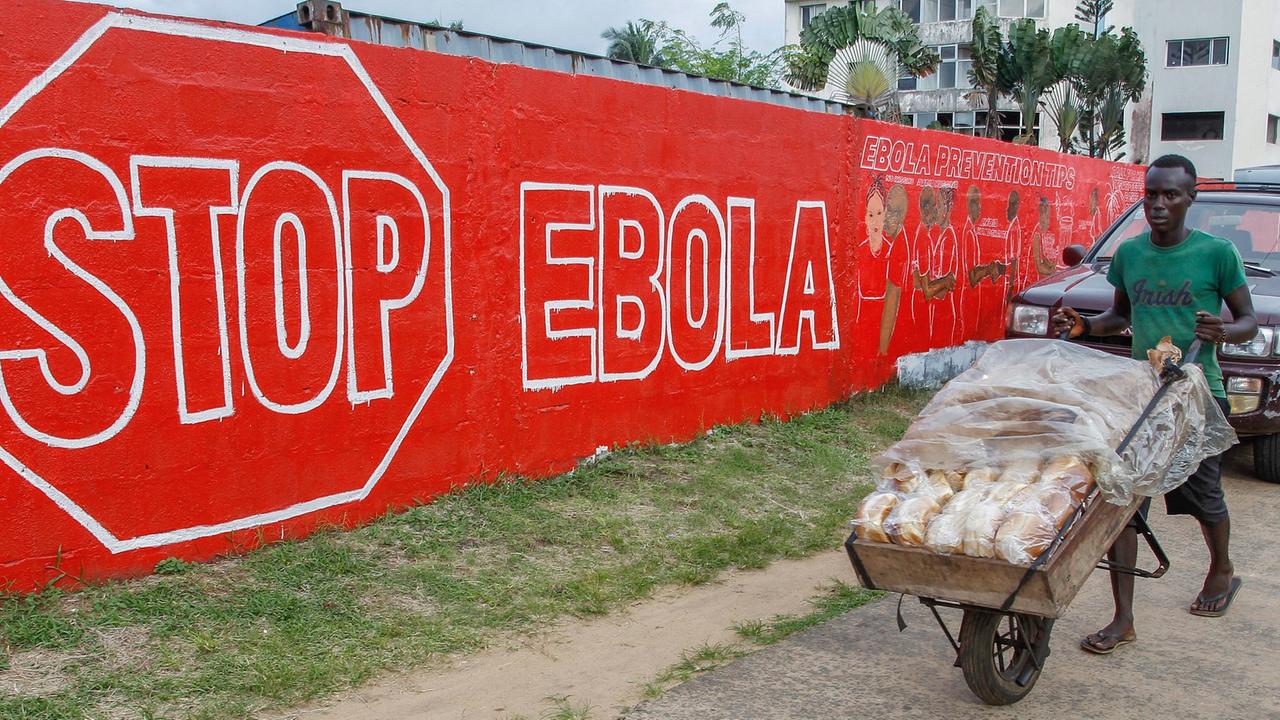 Ein Mann schiebt am 15. September 2014 in der liberianischen Hauptstadt Monrovia eine Karre mit Brot über eine Straße. Im Hintergrund hängt ein Schild mit der Aufschrift Stop Ebola. Ein Mann schiebt am 15. September 2014 in der liberianischen Hauptstadt Monrovia eine Karre mit Brot über eine Straße. Im Hintergrund hängt ein Schild mit der Aufschrift Stop Ebola.
