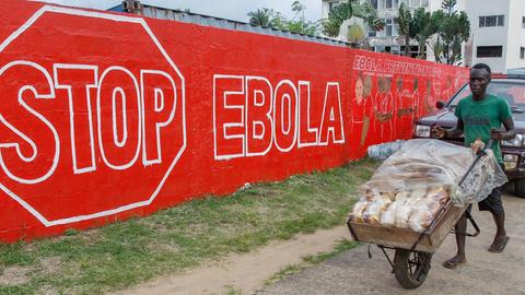 Ein Mann schiebt am 15. September 2014 in der liberianischen Hauptstadt Monrovia eine Karre mit Brot über eine Straße. Im Hintergrund hängt ein Schild mit der Aufschrift Stop Ebola.