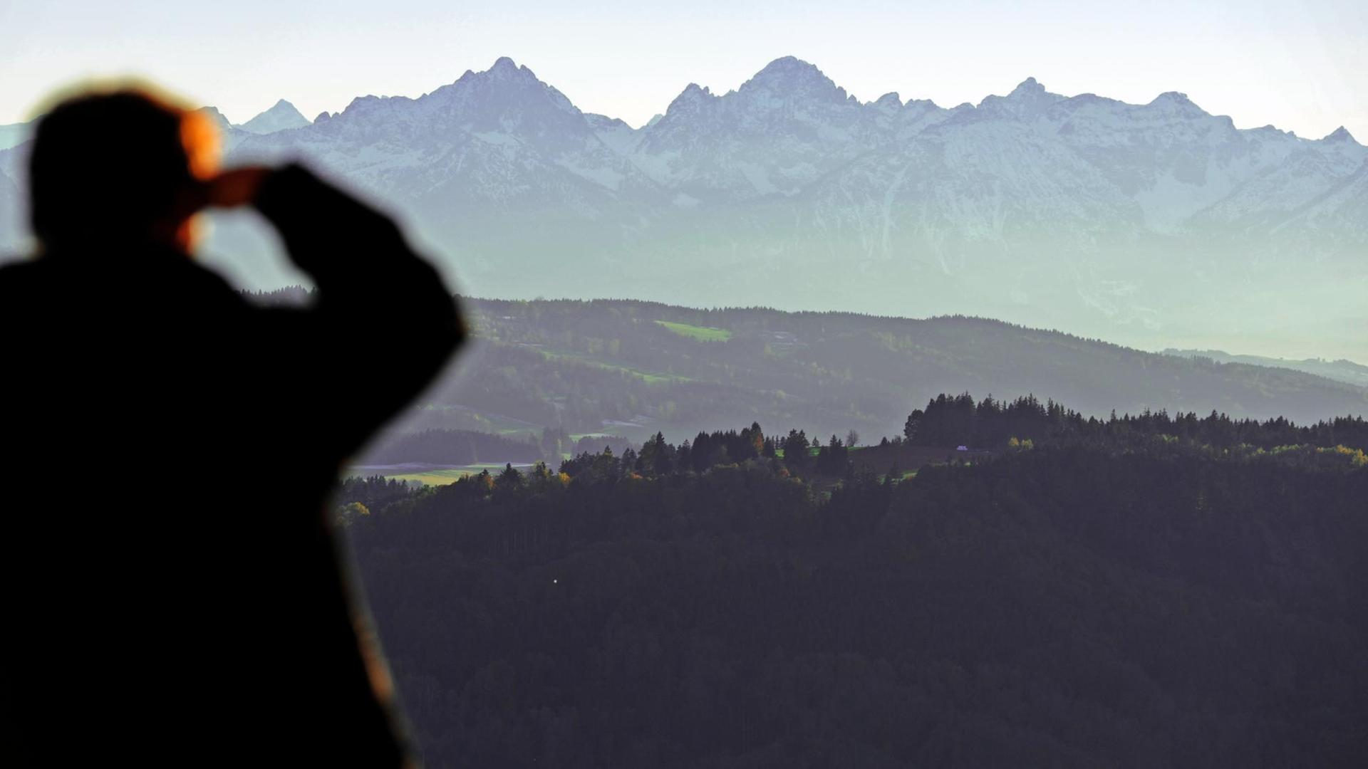 Ein Mann, der sich mit der rechten Hand vor dem Sonnenlicht schützt, schaut von Hohenpeißenberg aus auf die Alpen. Ein Mann, der sich mit der rechten Hand vor dem Sonnenlicht schützt, schaut von Hohenpeißenberg aus auf die Alpen.