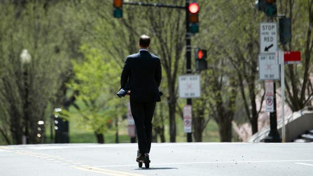 Ein Mann fährt im Anzug auf seinem Elektroroller über eine Hauptstrasse in Washington DC.