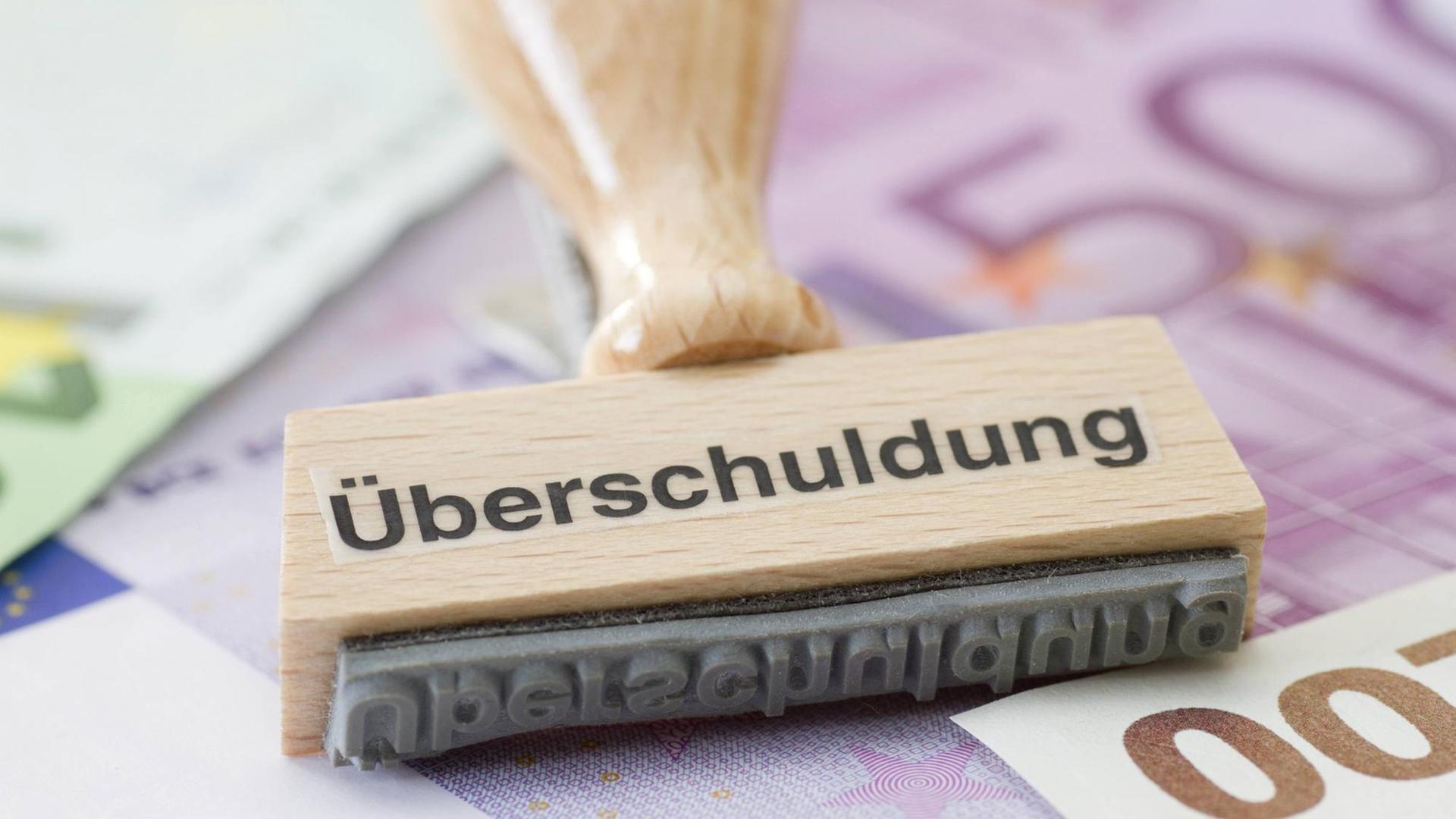 Ein Stempel mit Aufschrift Überschuldung vor Geldscheinen. Ein Stempel mit Aufschrift Überschuldung vor Geldscheinen.
