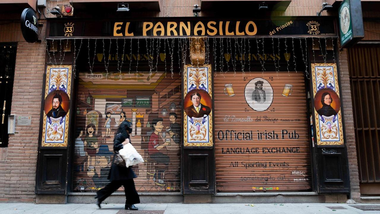 Eine Frau mit Mundschutz geht inmitten der Corona-Pandemie an einem geschlossenen Restaurant in Madrid vorbei.