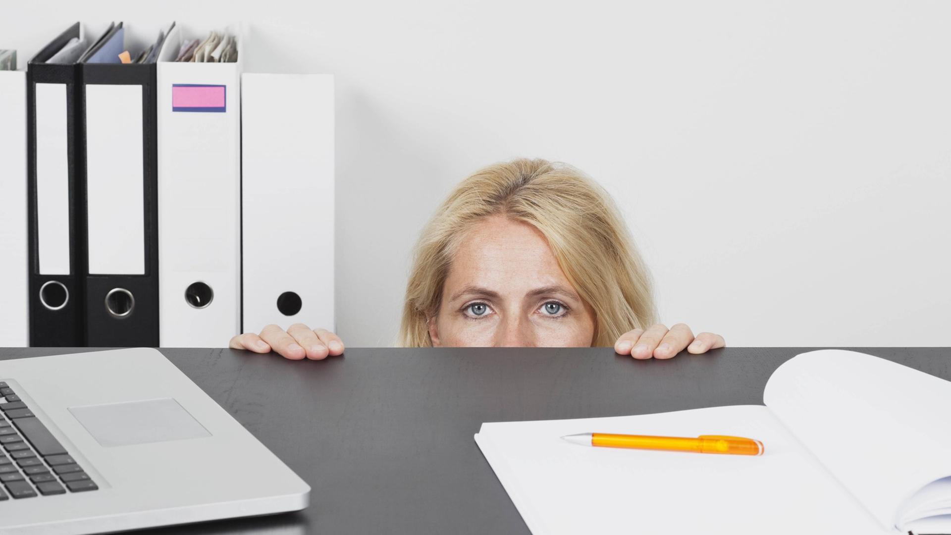 Eine Frau versteckt sich hinter einem Schreibtisch im Büro