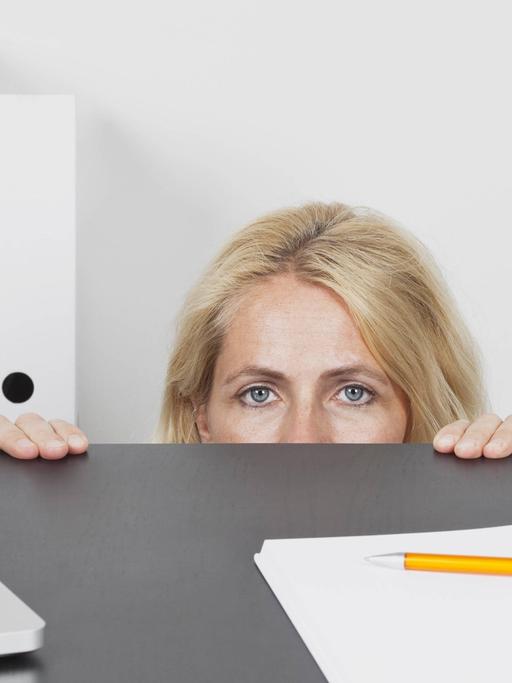 Eine Frau versteckt sich hinter einem Schreibtisch im Büro