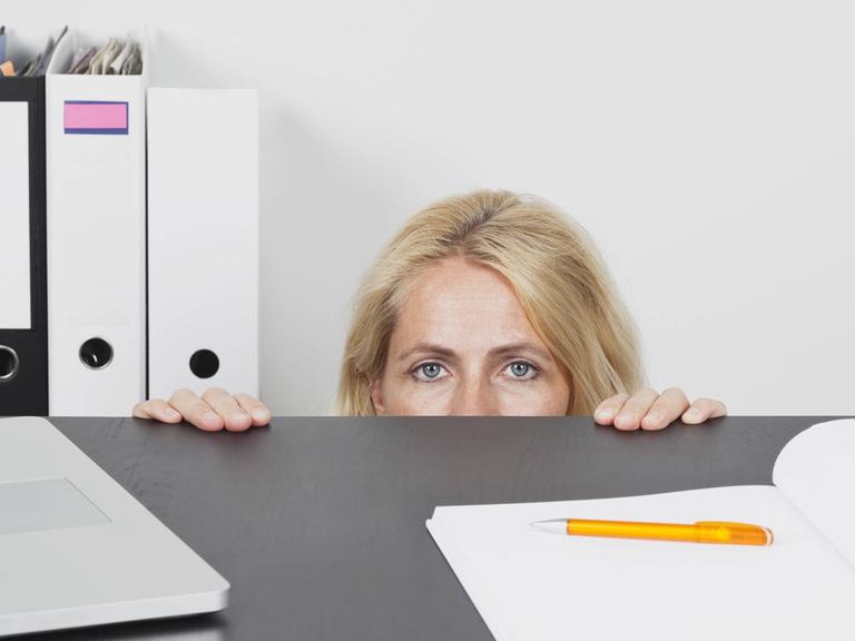 Eine Frau versteckt sich hinter einem Schreibtisch im Büro
