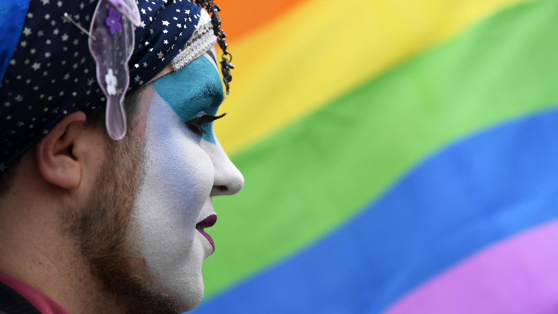Bärtiger geschminkter Mann im Profil vor einer Regenbogenflagge. Bärtiger geschminkter Mann im Profil vor einer Regenbogenflagge.