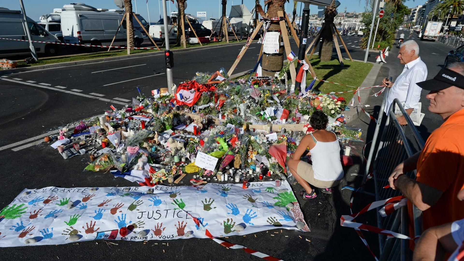 Sie sehen viele Blumen und ein Transparent mit bunten Handabdrücken auf der Uferstraße in Nizza. Sie sehen viele Blumen und ein Transparent mit bunten Handabdrücken auf der Uferstraße in Nizza.