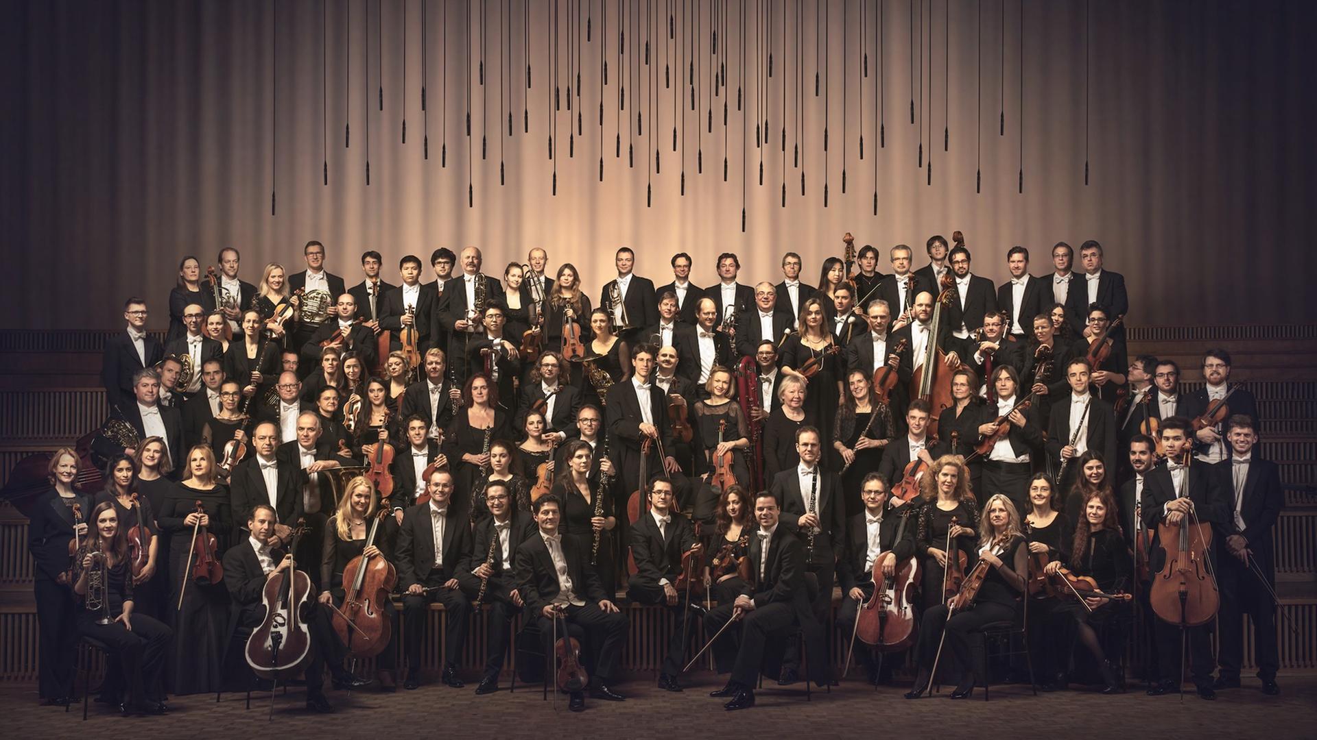 Das Rundfunk Sinfonieorchester Berlin steht auf der Bühne unter einem Mikrophonhimmel Das Rundfunk Sinfonieorchester Berlin steht auf der Bühne unter einem Mikrophonhimmel