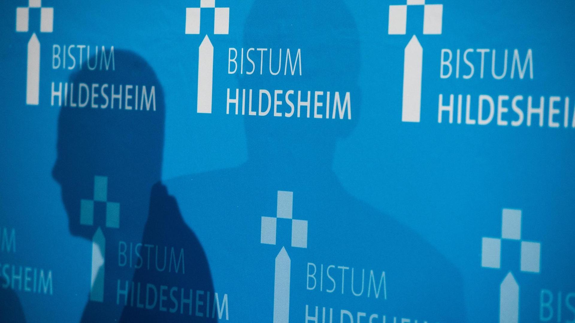Bei einer Pressekonferenz sind Schatten auf einer Wand mit dem Aufdruck "Bistum Hildesheim".
