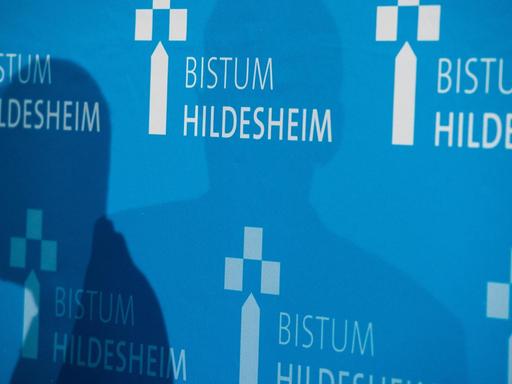 Bei einer Pressekonferenz sind Schatten auf einer Wand mit dem Aufdruck "Bistum Hildesheim".