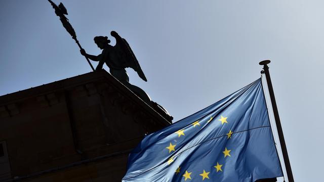 Eine Europa-Fahne weht am 08.11.2014 vor dem Brandenburger Tor in Berlin, auf dem die Figur der Siegesgöttin Viktoria als Silhouette zu sehen ist