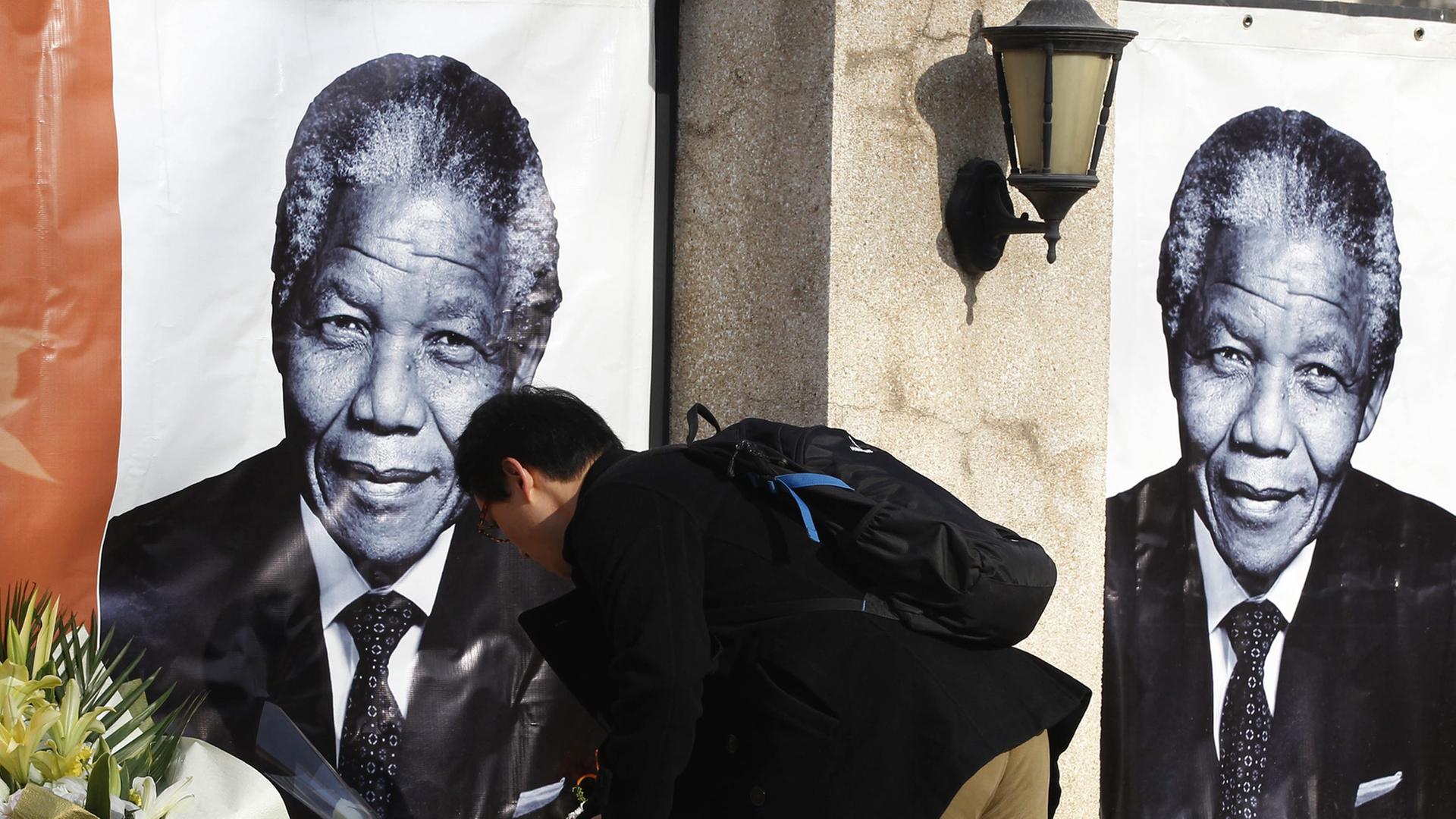 Ein Mann legt Blumen vor Postern mit dem Porträt Nelson Mandelas nieder. Ein Mann legt Blumen vor Postern mit dem Porträt Nelson Mandelas nieder.
