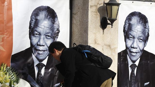 Ein Mann legt Blumen vor Postern mit dem Porträt Nelson Mandelas nieder.