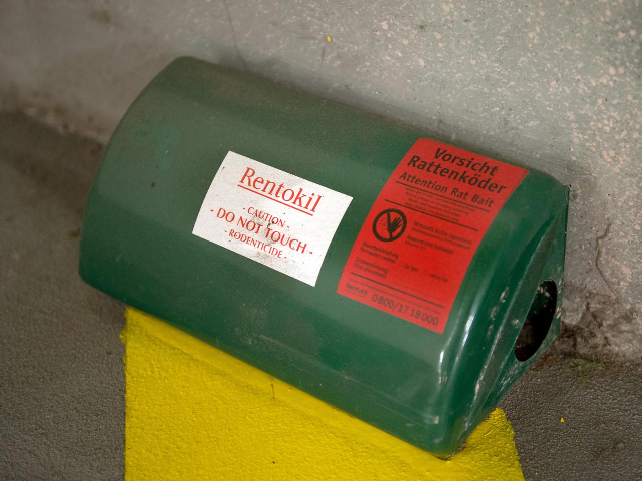 Eine grüne Box mit einem Loch an der Seite steht auf einem Asphaltboden, oben ein Aufkleber mit der Aufschrift "Vorsicht Rattenköder" Eine grüne Box mit einem Loch an der Seite steht auf einem Asphaltboden, oben ein Aufkleber mit der Aufschrift "Vorsicht Rattenköder"