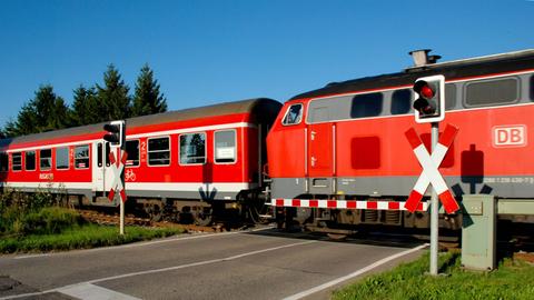 Ein Nahverkehrszug der Deutschen Bahn mit Diesellok fährt über einen Bahnübergang in Bayern.