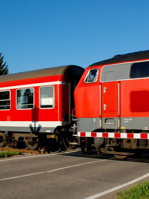 Ein Nahverkehrszug der Deutschen Bahn mit Diesellok fährt über einen Bahnübergang in Bayern.