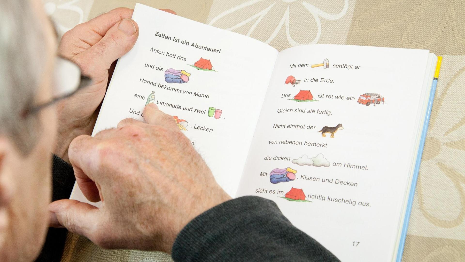 Die Finger eines älteren Mannes gleiten über die Zeilen eines Buchs für Leseanfänger. Die Finger eines älteren Mannes gleiten über die Zeilen eines Buchs für Leseanfänger.