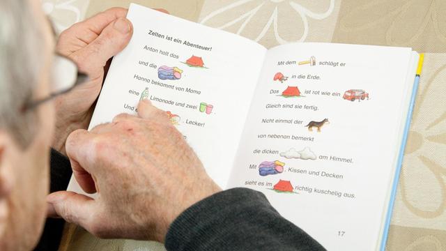 Die Finger eines älteren Mannes gleiten über die Zeilen eines Buchs für Leseanfänger.