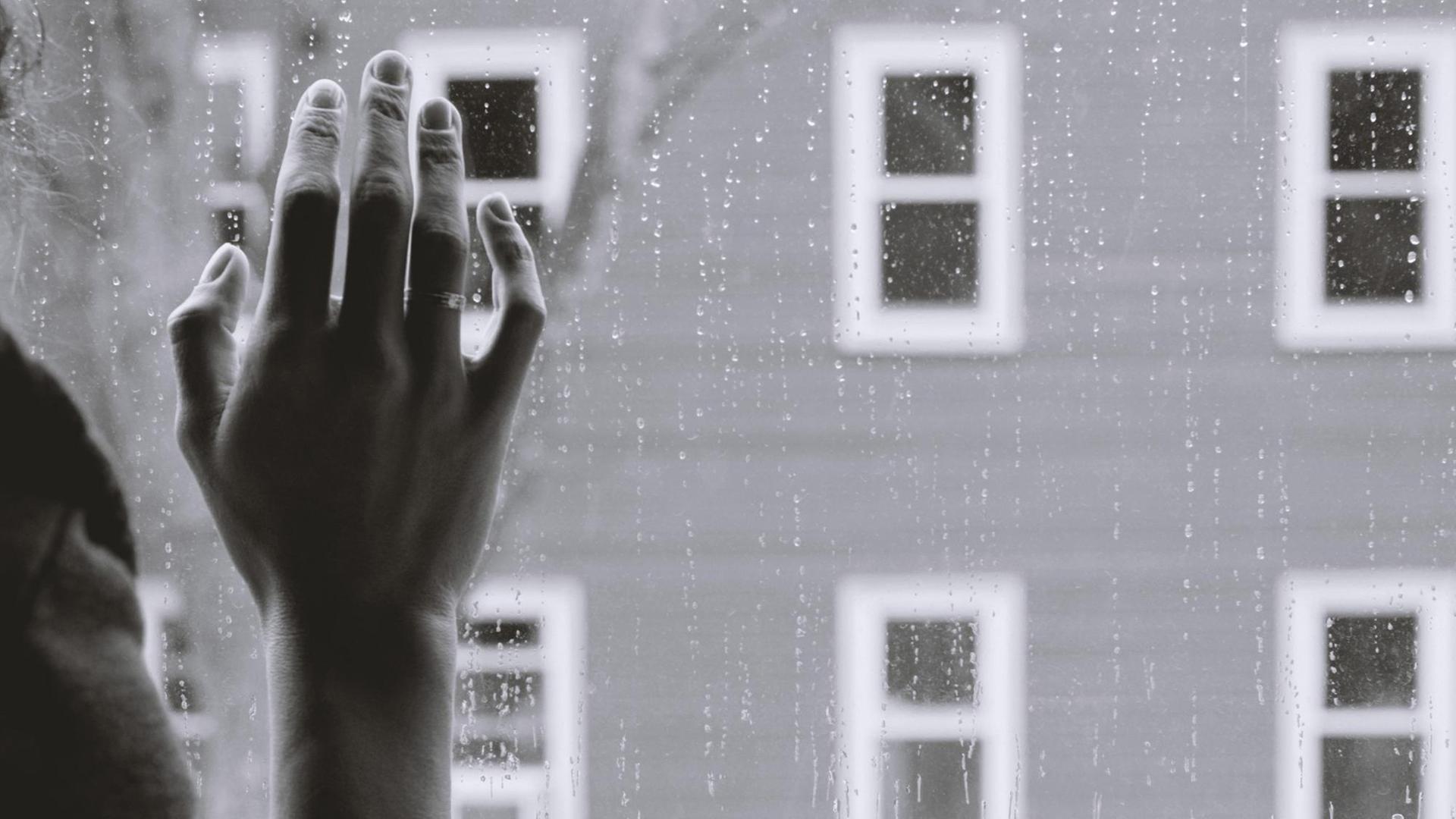Melancholisches Schwarzweiß-Foto einer Hand, die auf einem Fenster liegt. Melancholisches Schwarzweiß-Foto einer Hand, die auf einem Fenster liegt.