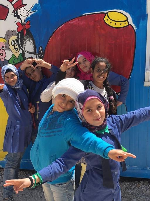 Syrische Kinder hüpfen vor einem bunt bemalten Container des Gemeinde-Zentrums, wo sie Hausaufgaben machen können.