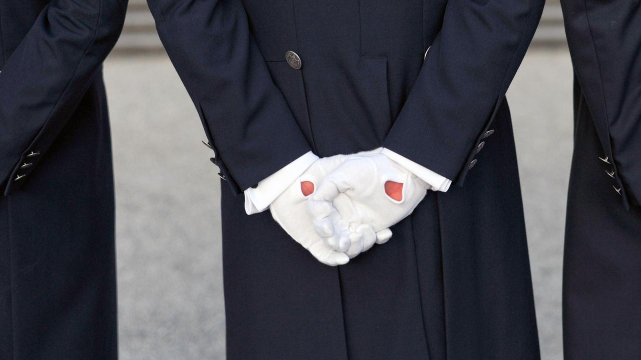 Ein Diener hält seine behandschuhten Hände hinter dem Rücken verschränkt. Ein Diener hält seine behandschuhten Hände hinter dem Rücken verschränkt.