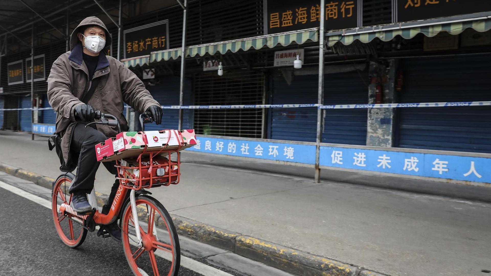 Ein Mann trägt eine Maske, während er auf einem Mobike an dem geschlossenen Huanan-Großmarkt für Meeresfrüchte vorbeifährt, der mit Fällen von Coronavirus in Verbindung gebracht wurde Ein Mann trägt eine Maske, während er auf einem Mobike an dem geschlossenen Huanan-Großmarkt für Meeresfrüchte vorbeifährt, der mit Fällen von Coronavirus in Verbindung gebracht wurde