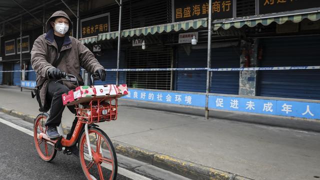 Ein Mann trägt eine Maske, während er auf einem Mobike an dem geschlossenen Huanan-Großmarkt für Meeresfrüchte vorbeifährt, der mit Fällen von Coronavirus in Verbindung gebracht wurde
