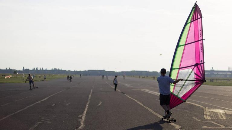 Ein Besucher fährt auf dem als Tempelhofer Freiheit bezeichneten ehemaligen Flughafen Tempelhof in Berlin mit einem Windsegel Longboard Ein Besucher fährt auf dem als Tempelhofer Freiheit bezeichneten ehemaligen Flughafen Tempelhof in Berlin mit einem Windsegel Longboard