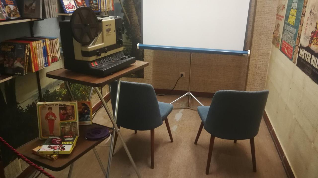 Zwei Stühle stehen neben einem Filmprojektor vor einer Leinwand