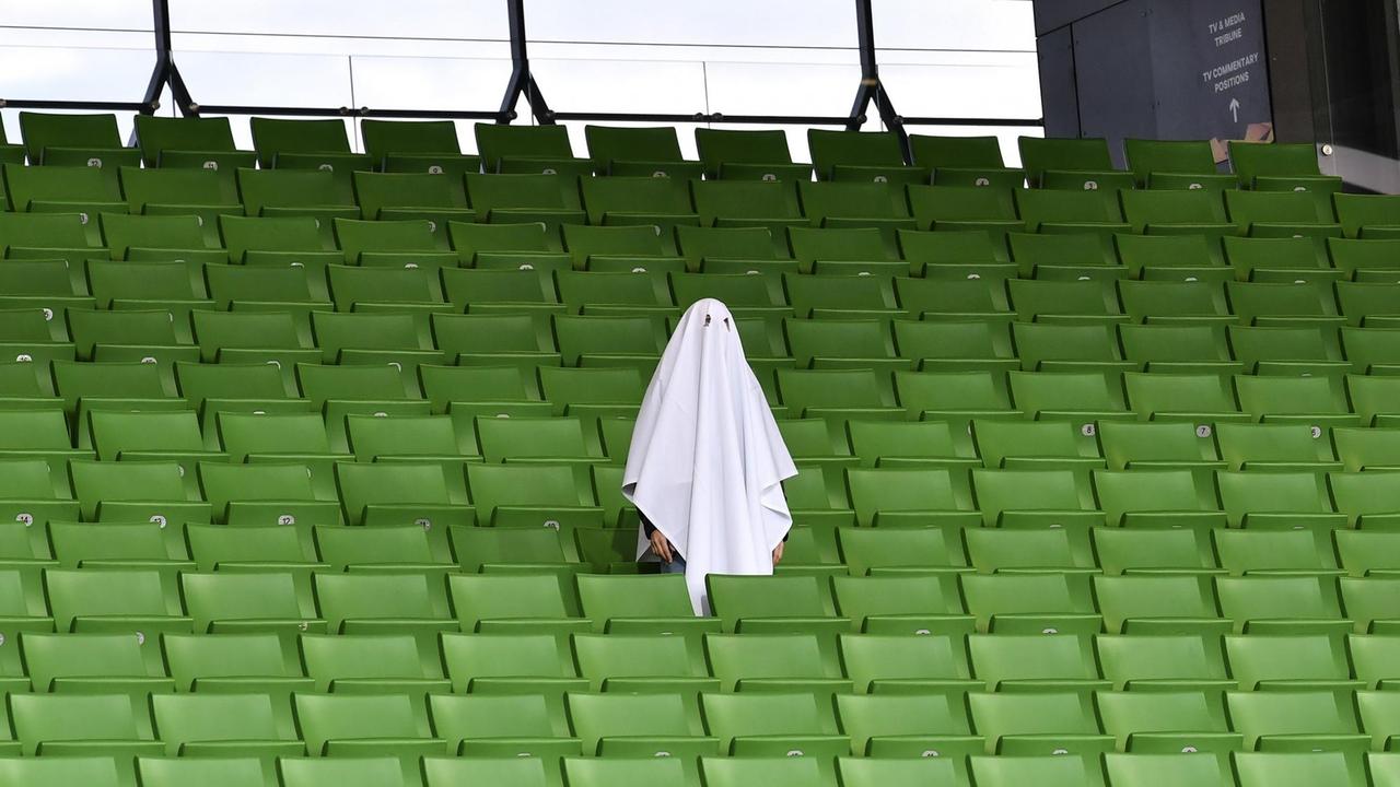 Ein als Geist gekleideter Mann steht auf einer leeren Zuschauertribüne im Stadion.