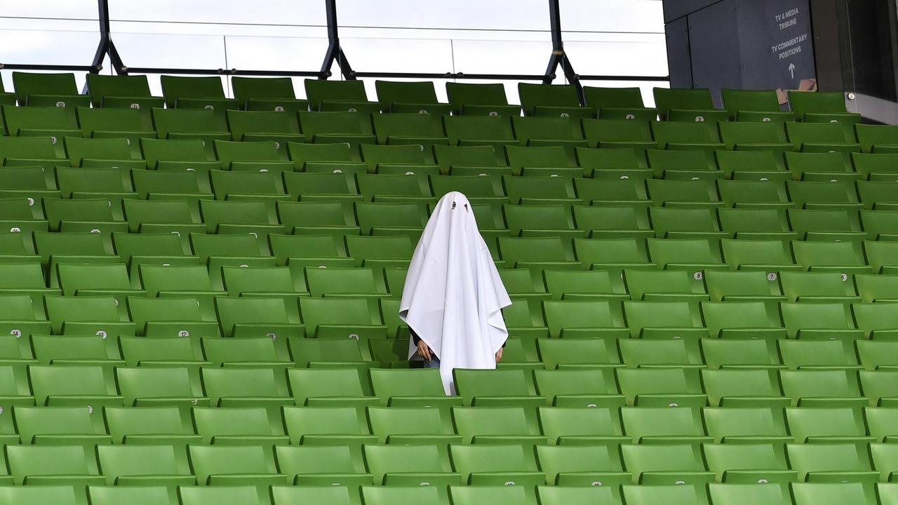 Ein als Geist gekleideter Mann steht auf einer leeren Zuschauertribüne im Stadion. Ein als Geist gekleideter Mann steht auf einer leeren Zuschauertribüne im Stadion.
