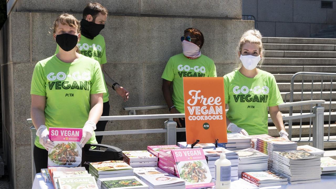 Junge Aktiivisten der Tierschutzorganisation PETA in grünen T-Shirts bieten kostenlose vegane Hot Dogs und Vegan-Kochbücher an. (5. August, 2020, Washington, DC)