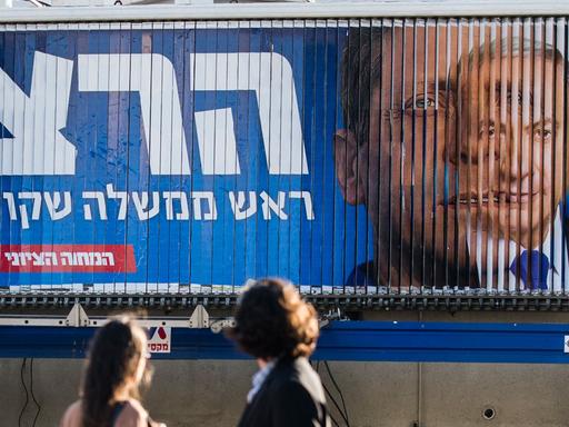Am 17. März wählen die Israelis vorzeitig ein neues Parlament: Wahlberechtigte stehen vor einer Videowand, auf der Regierungschef Netanjahu und Oppositionsführer Herzog zu sehen sind.