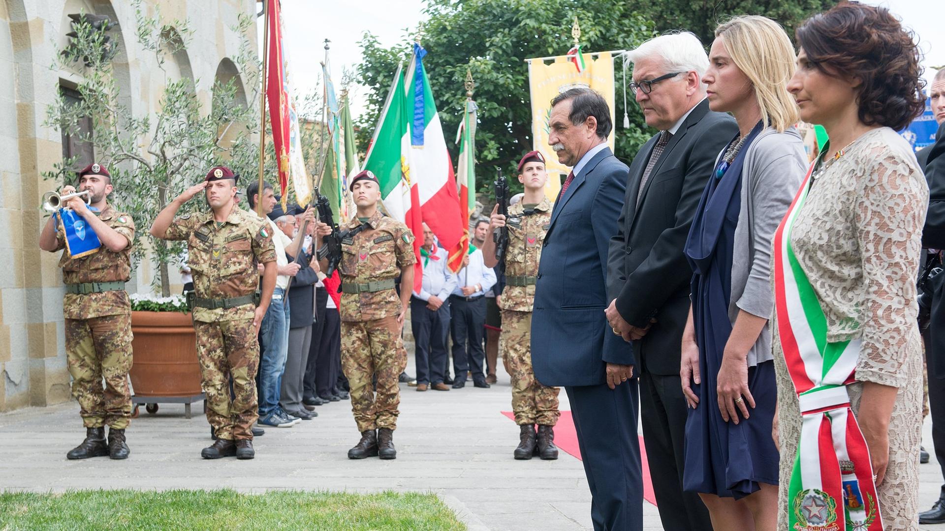 Steinmeier, Mogherini und Minchetti stehen an einem Grab, im Hintergrund salutieren Soldaten. Steinmeier, Mogherini und Minchetti stehen an einem Grab, im Hintergrund salutieren Soldaten.