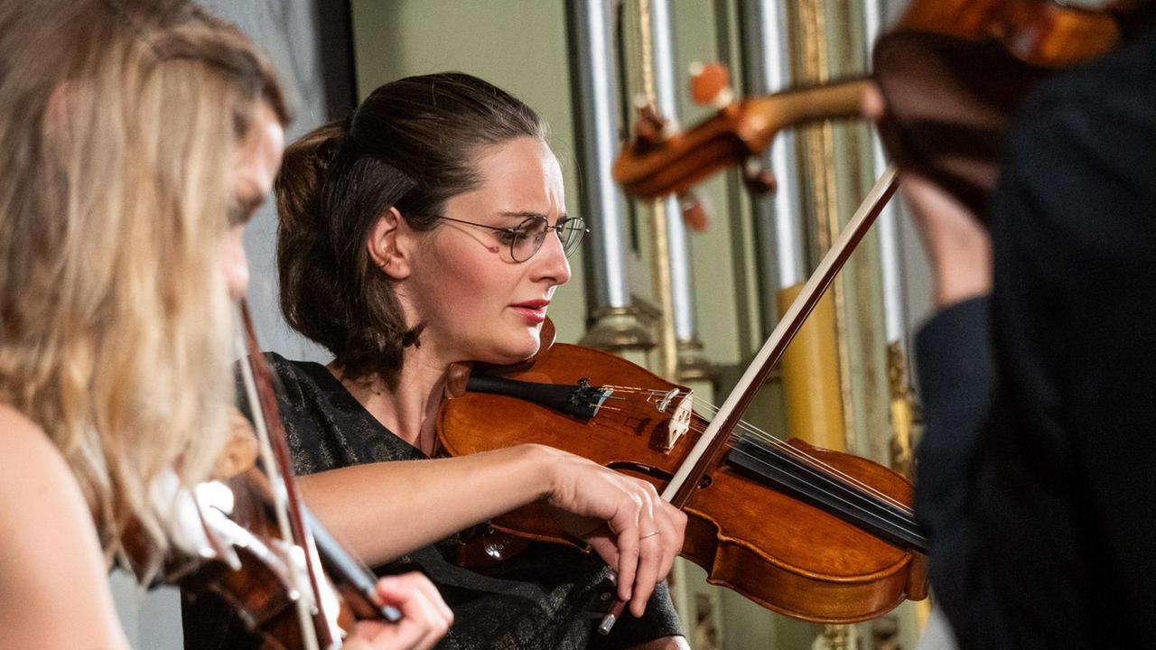Großaufnahme einer Geigerin, die zwischen anderen Musikern spielt. Großaufnahme einer Geigerin, die zwischen anderen Musikern spielt.