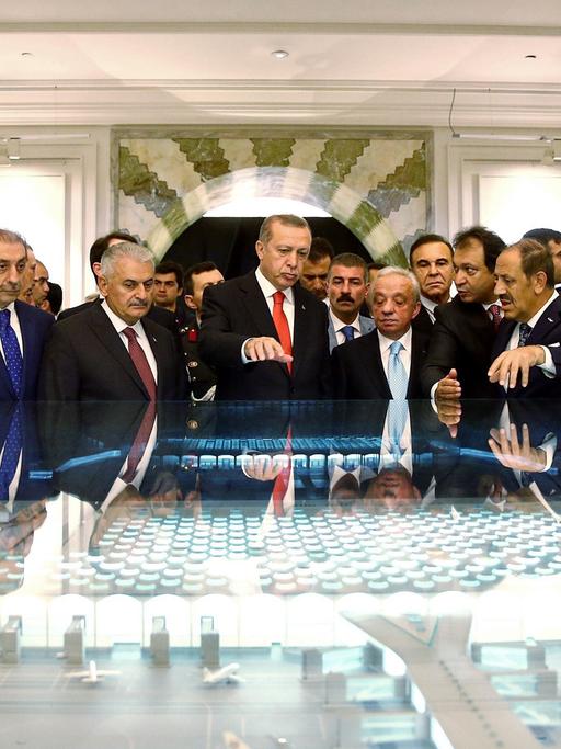 Der türkische Präsident Recep Tayyip Erdogan steht in einer Gruppe von Männern bei der Unterschriften-Zeremonie der "Istanbul New Airport Project Financing" am 19.10.2015 in Istanbul vor einem großen Modell des Flughafens.