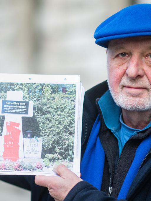 Der Aktionskünstler Wolfram Kastner vor Beginn seines Prozesses im Landgericht in München. Er zeigt ein Foto, auf dem das Denkmal für den als Kriegsverbrecher hingerichteten General A. Jodl auf der Fraueninsel im Chiemsee zu sehen ist. Kastner hatte das Denkmal unter anderem mit einer Hinweistafel mit der Aufschrift "Keine Ehre für einen Kriegsverbrecher" und roter Farbe als Symbol für das von ihm vergossene Blut versehen.