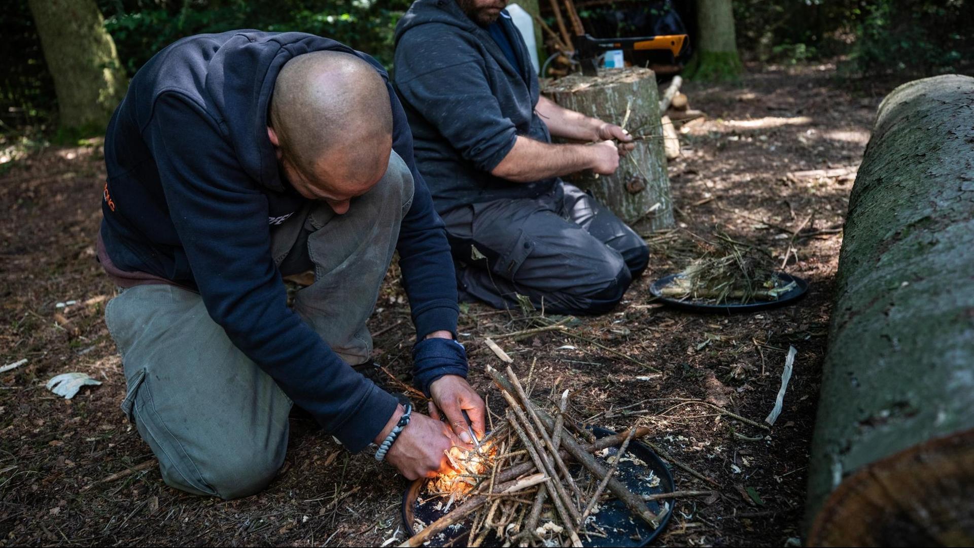 Teilnehmende eines Survivalkurses entfachen ein Feuer Teilnehmende eines Survivalkurses entfachen ein Feuer